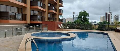 A rooftop swimming pool with a circular design, surrounded by a low fence and a building with multiple balconies in the background.