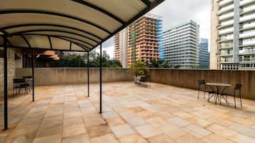 Un patio al aire libre con suelo de piedra, una zona cubierta y varias mesas y sillas.