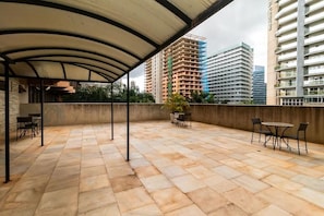 Un patio al aire libre con suelo de piedra, una zona cubierta y varias mesas y sillas.