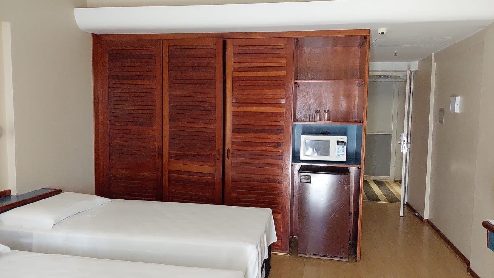 A hotel room with a bed, a wardrobe, a microwave, and a refrigerator.