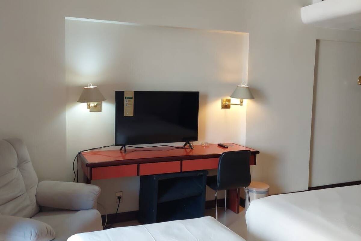 A hotel room with a bed, a desk with a computer, a chair, and a TV.