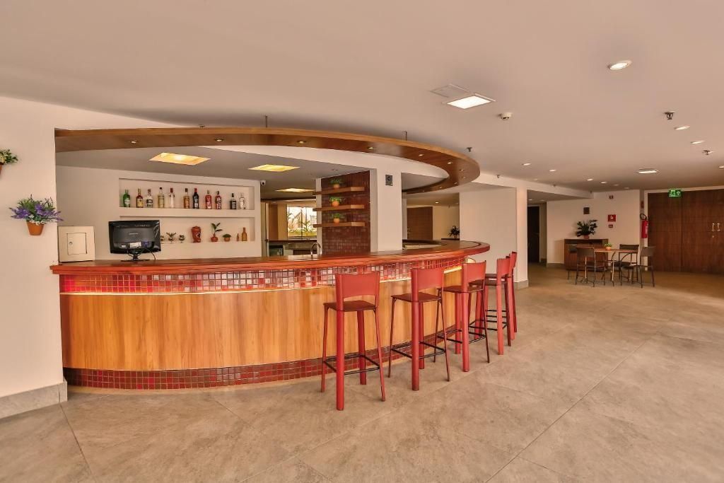 Zona de bar con una barra curva, taburetes rojos y una pared que exhibe varias botellas.