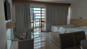 Une chambre d’hôtel avec une table à manger en verre, un canapé, un lit et un balcon doté de rideaux.