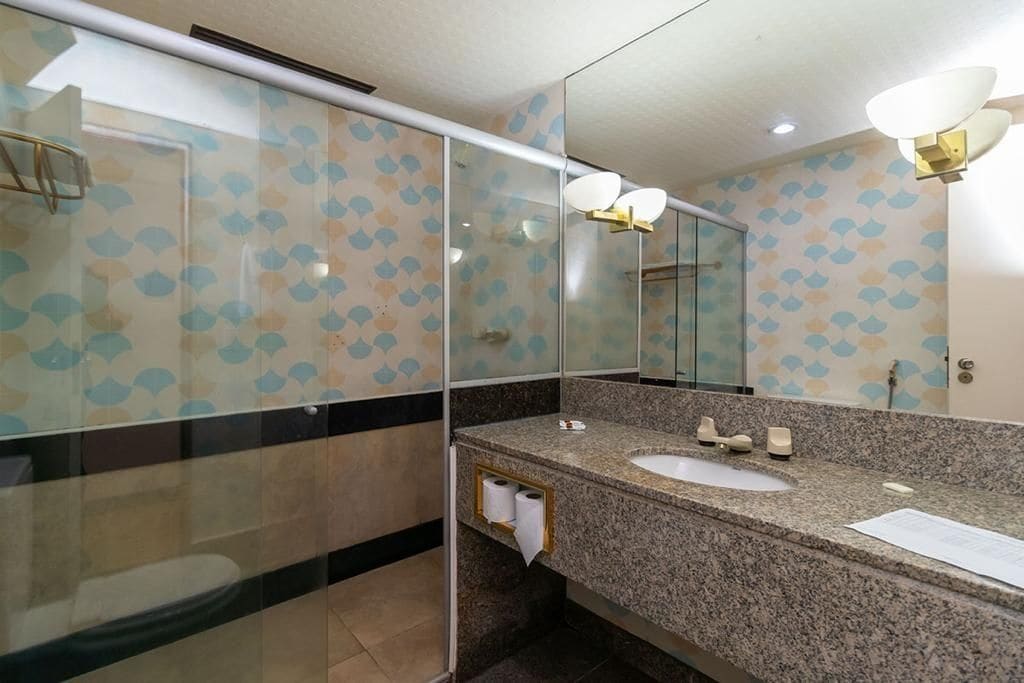 A bathroom with a granite countertop, two sinks, a mirror, and a glass shower enclosure.
