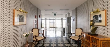 Un'hall d'albergo con pavimento a scacchi, carta da parati decorata e arredi classici.