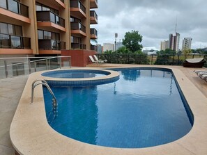 A rectangular swimming pool with a tiled edge, surrounded by a beige deck. - Kubitschek Hotel Flat Particular (Brasília)