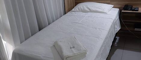Une chambre d’hôtel avec un lit bien fait, une table de chevet avec un téléphone et une prise électrique au mur.
