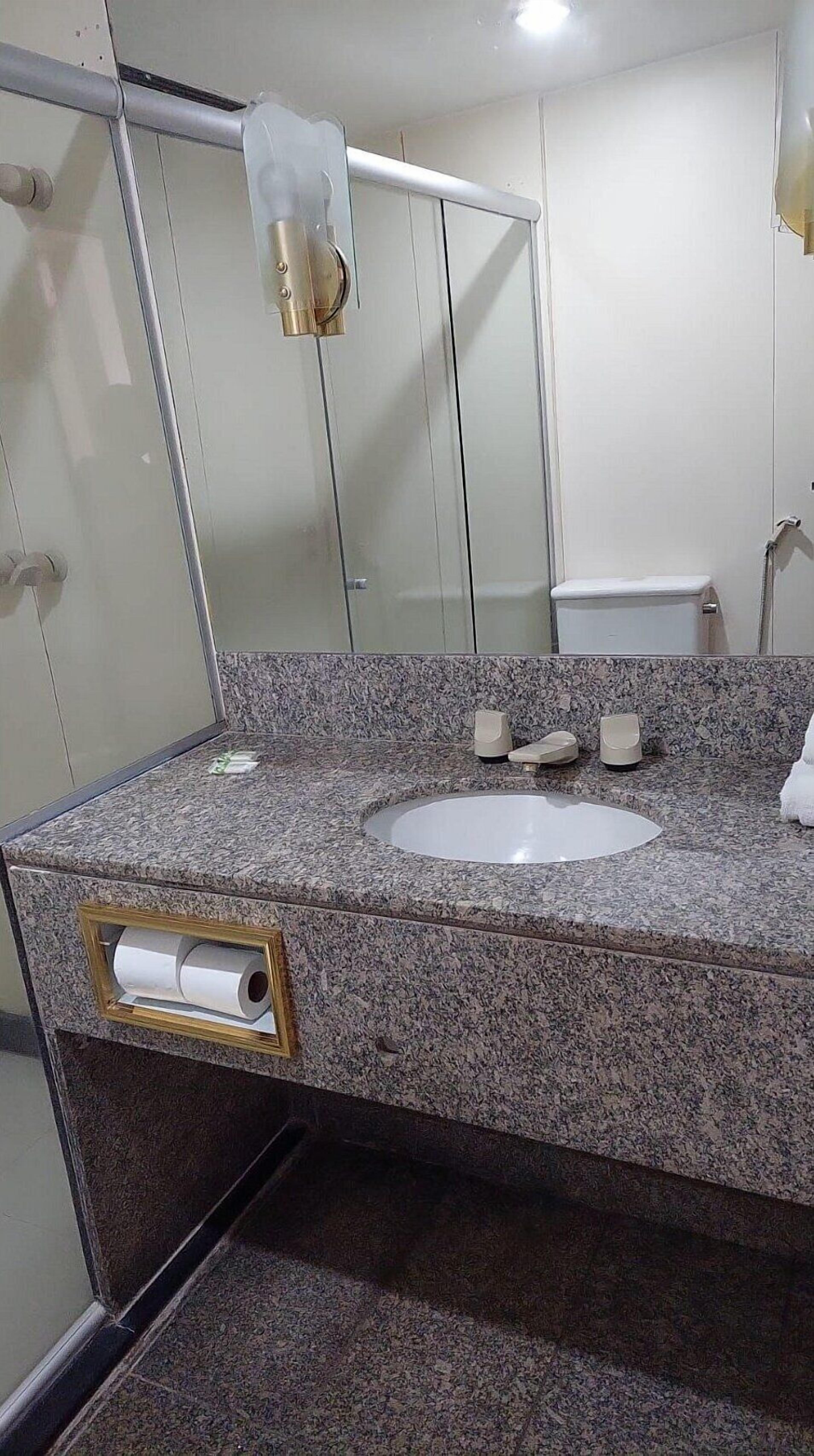 A bathroom with a granite countertop, a sink, a toilet, and a mirror.