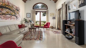A spacious living room with a high ceiling, a large window, a television, and a seating area with a sofa and chairs. - Villa Casale-Villa in Sicily with pool and sea views (Arcieri - Isolotto)