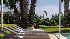 A poolside area with lounge chairs, a small table with fruit and a drink, and a view of the pool. - Villa Casale-Villa in Sicily with pool and sea views (Arcieri - Isolotto)