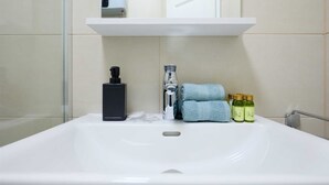 A bathroom with a white sink, a black soap dispenser, a bottle of olive oil, and a blue towel. - Dominium Premium Location Suites Studio apartment (Dubrovnik)