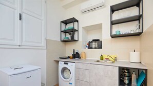 A compact kitchen with a washing machine, a coffee maker, and a microwave. - Dominium Premium Location Suites Studio apartment (Dubrovnik)