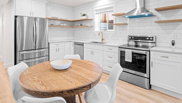 Una cocina moderna con armarios blancos, electrodomésticos de acero inoxidable y una mesa de comedor de madera.