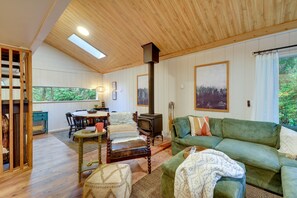 A cozy living room with a wooden ceiling, a fireplace, a green sofa, and a dining area with a table and chairs.