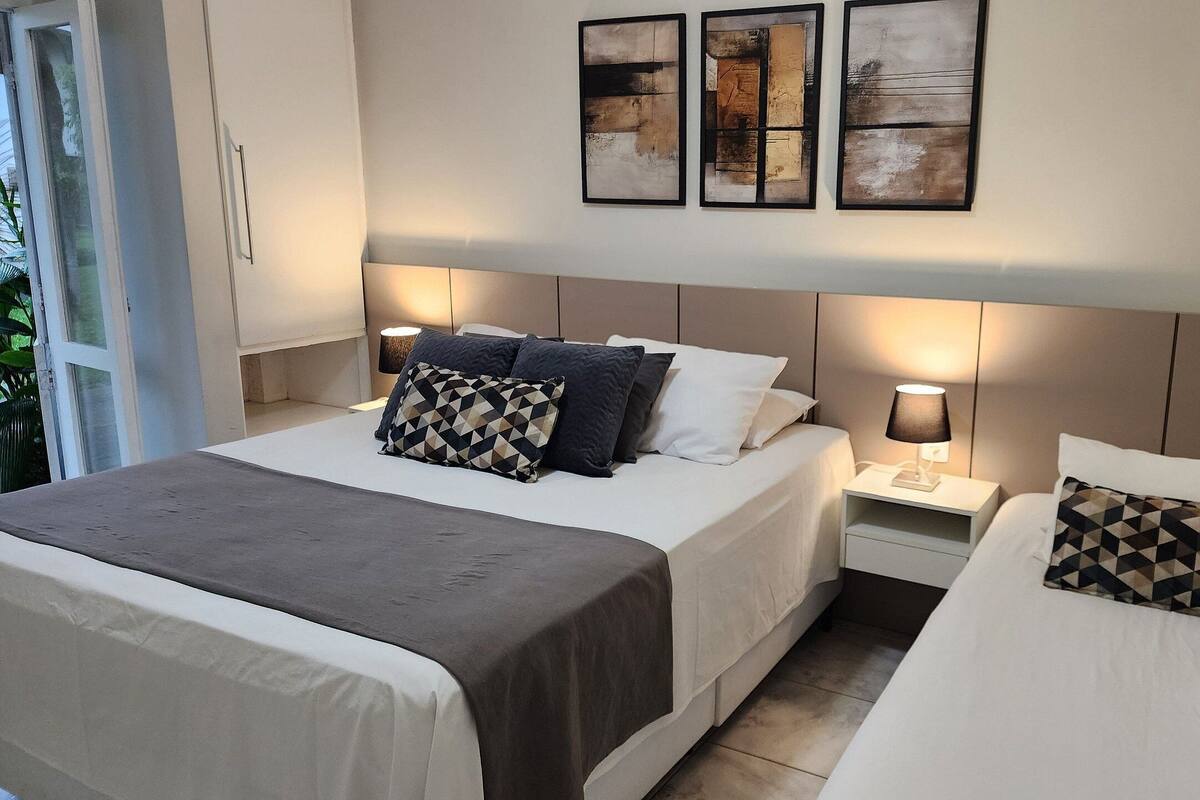 A hotel room with a large bed, two bedside tables, and three wall-mounted artworks.