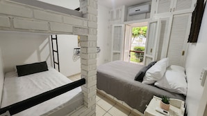 A room with a bunk bed, a single bed, a small table with a plant, and a window with shutters. - Angra Temporada (Angra dos Reis)
