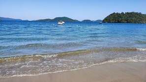 Una playa con agua cristalina, un bote y colinas a la distancia.