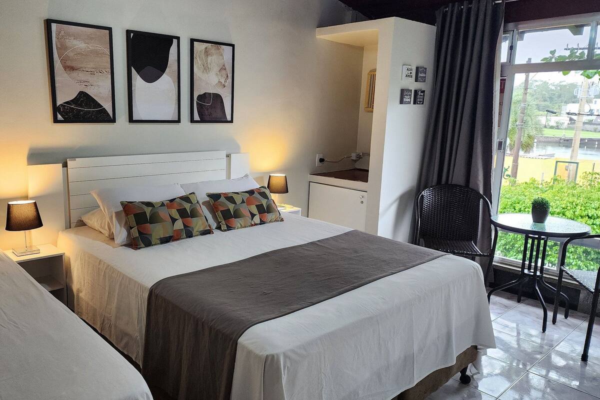 A hotel room with a bed, bedside tables, a small desk, a chair, and a window with a view.