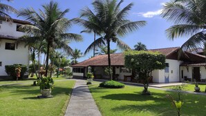 A courtyard with palm trees, a pathway, and a building with a tiled roof. - Angra Temporada (Angra dos Reis)