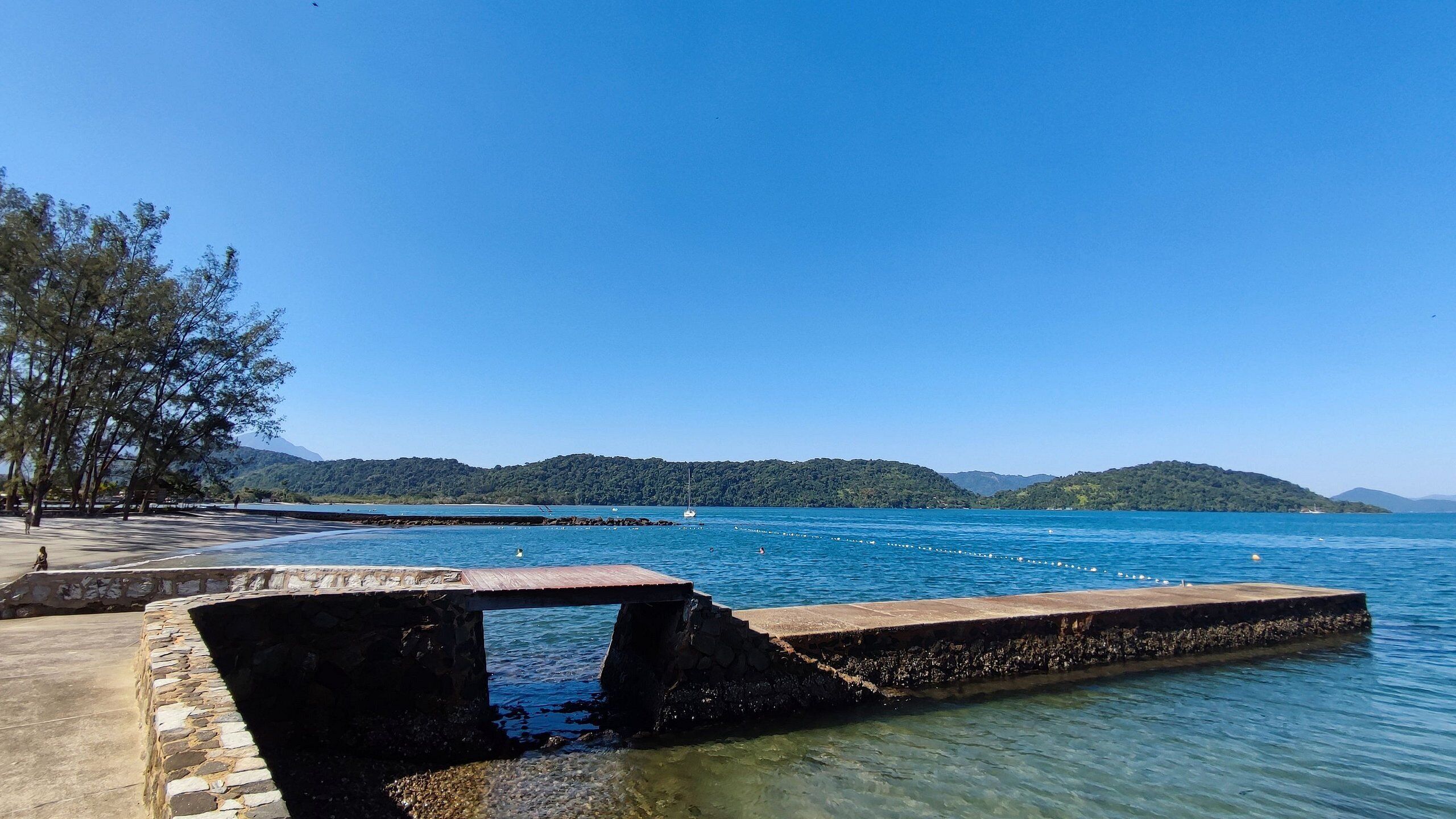 A clear view of a waterfront area with a stone pier, calm water, and distant green hills.