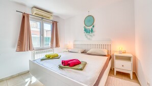 A bedroom with a bed, a bedside table with a lamp, a dreamcatcher on the wall, and an air conditioning unit. - House with pool Casa Kerchner in Alcudia (Alcúdia)