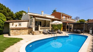 A swimming pool with lounge chairs, a stone wall, and a covered patio area. - House with pool Casa Kerchner in Alcudia (Alcúdia)