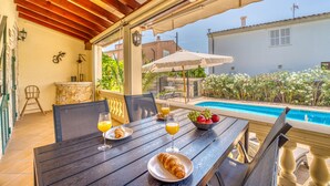 A covered outdoor dining area with a pool view, a table with breakfast items, and a stone wall. - House with pool Casa Kerchner in Alcudia (Alcúdia)