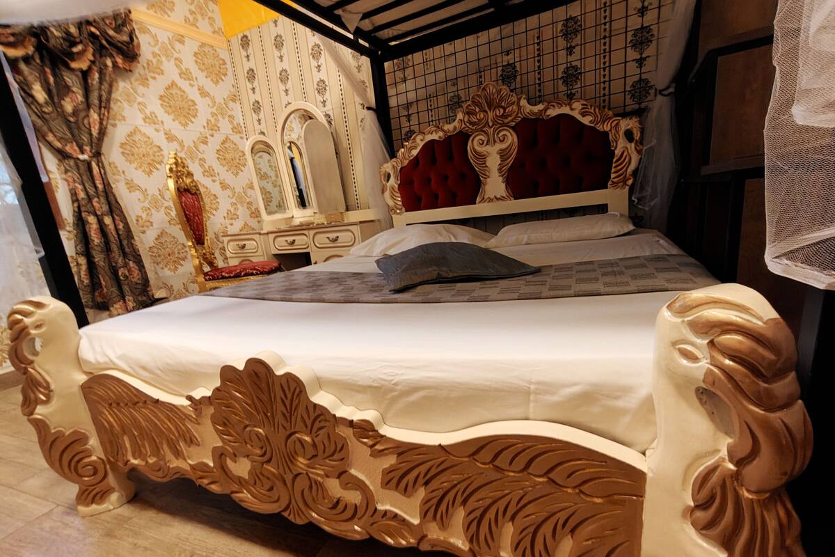 A bed with ornate carvings, a red upholstered headboard, and a mirror above it.