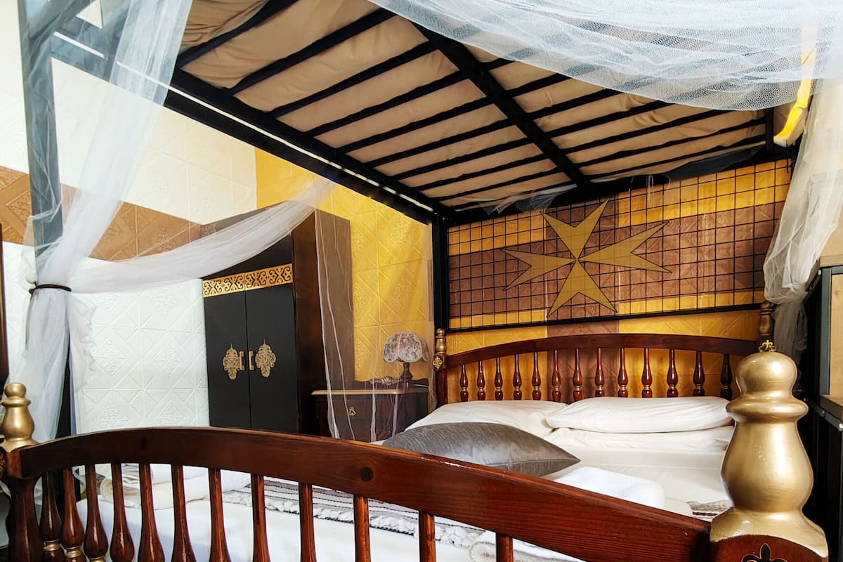 A wooden bed with a canopy, a decorative headboard, and a wall with a geometric pattern.