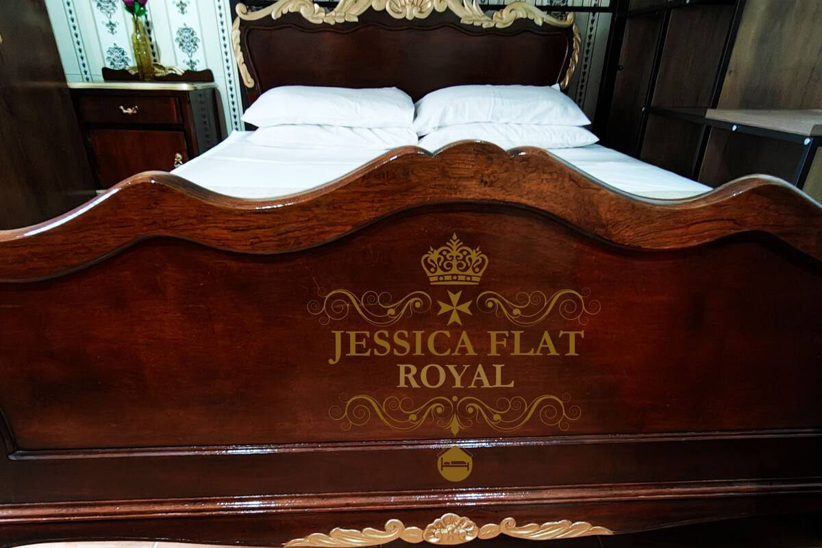 A bed with a wooden headboard, a floral vase, and a patterned wallpaper in the background.