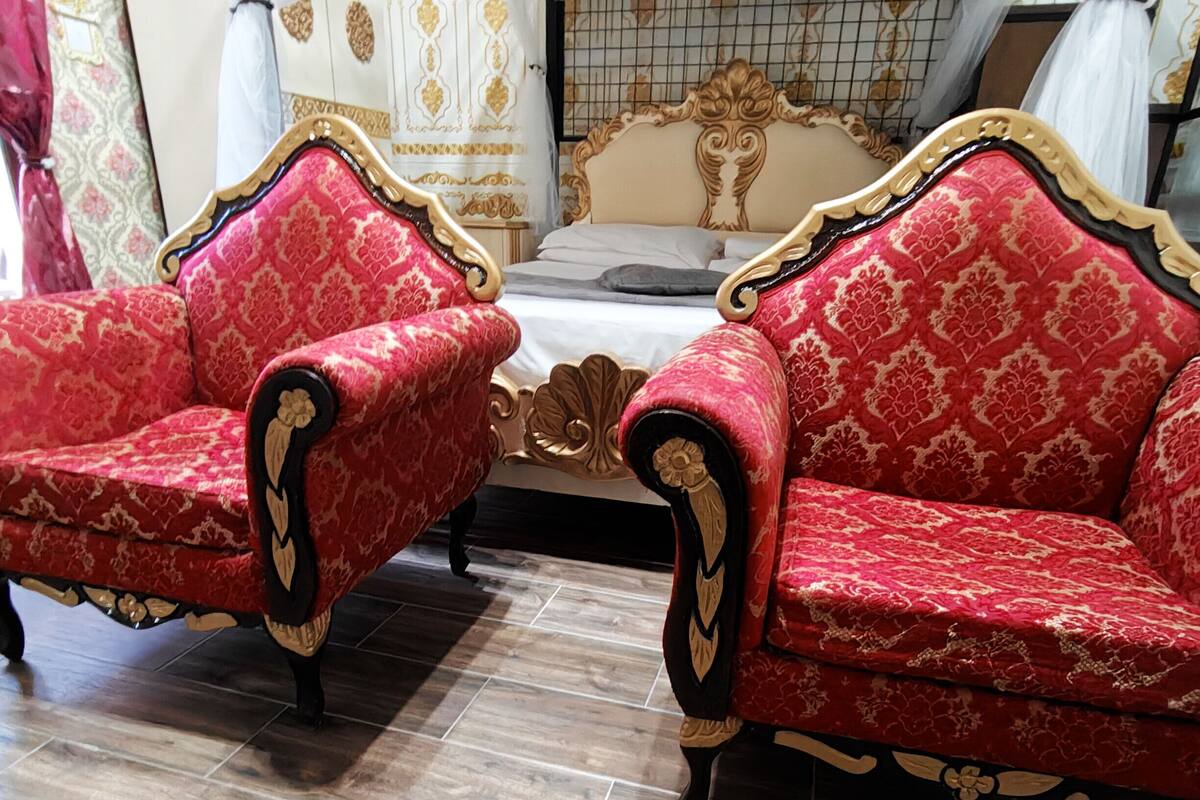 A room with two ornate red sofas with gold detailing, a bed with a white and gold headboard, and a tiled floor.