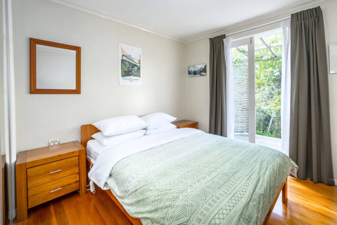 A bedroom with a bed, wooden nightstands, a dresser, a window with curtains, and wall art.