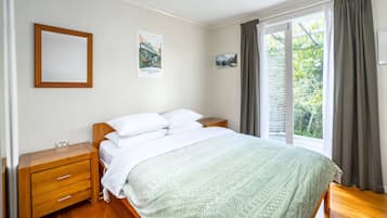 A bedroom with a bed, wooden nightstands, a dresser, a window with curtains, and wall art.