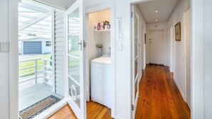 Un pasillo con suelo de madera, paredes blancas y una puerta que da a un área de lavandería con lavadora y estanterías.