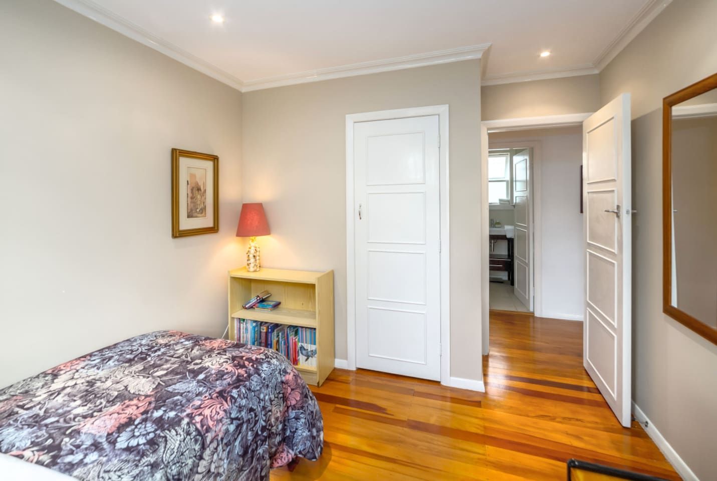 Une chambre à coucher comprenant un lit, une table de chevet avec une lampe, une bibliothèque et une porte donnant sur une salle de bain.