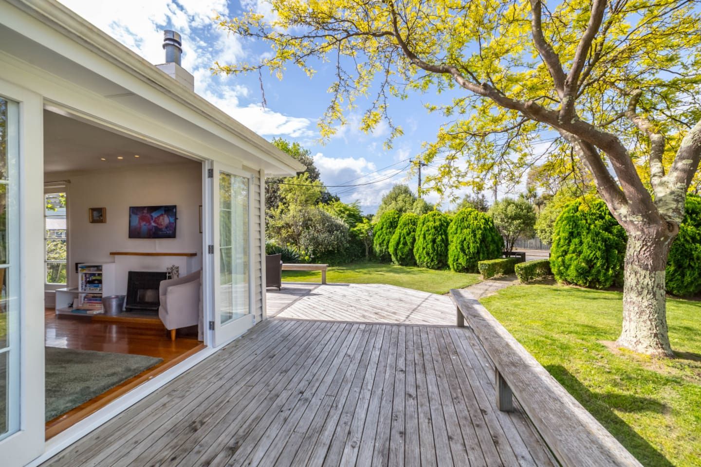 A modern house with a wooden deck, a fireplace, and a large glass door leading to a living room.