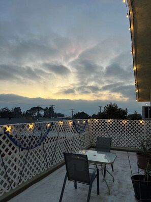 An outdoor patio with a table and chairs, a white lattice fence, and string lights.