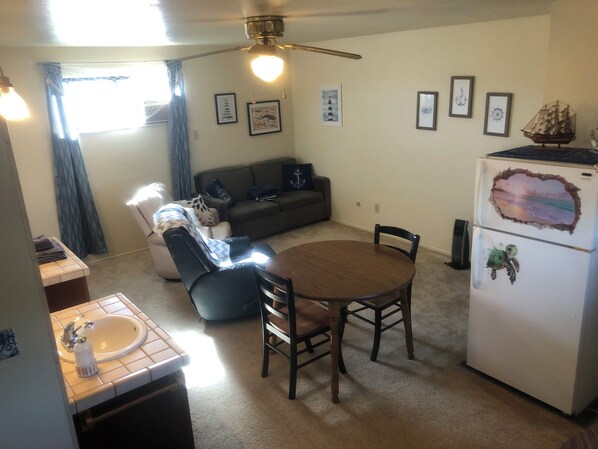 A compact living space with a kitchenette, a dining table, a sofa, and a ceiling fan.
