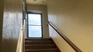 A carpeted staircase with a wooden handrail, leading to a door with a window at the top. - Cozy nautical-themed studio with private entrance (San Diego)
