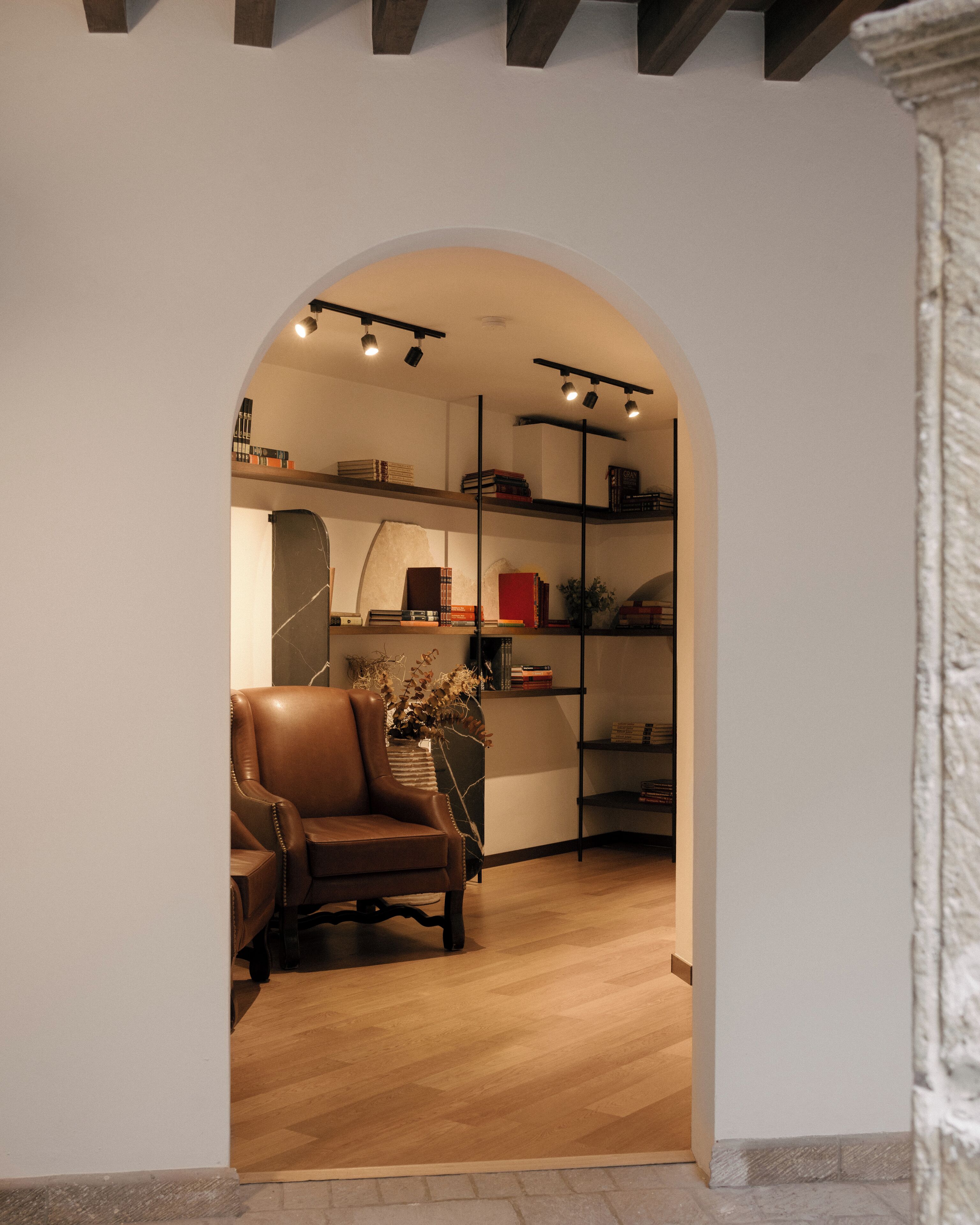 An interior space with a wooden floor, a leather armchair, and a bookshelf with books and decorative items.