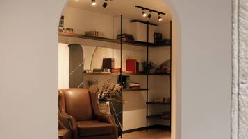 An interior space with a wooden floor, a leather armchair, and a bookshelf with books and decorative items.