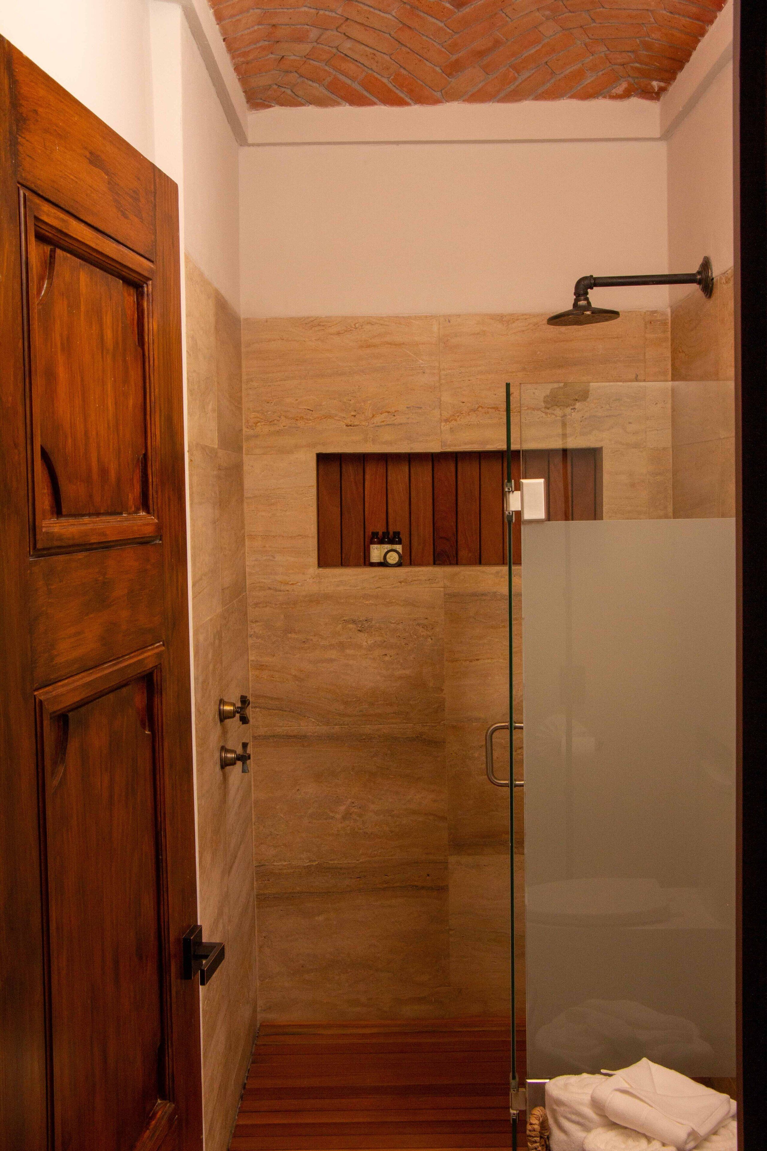 Un baño moderno con puerta de madera, cabina de ducha de vidrio y un pequeño estante de madera con artículos de tocador.