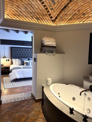 A modern bathroom with a large bathtub, a wooden ceiling, and a neatly made bed with a headboard.