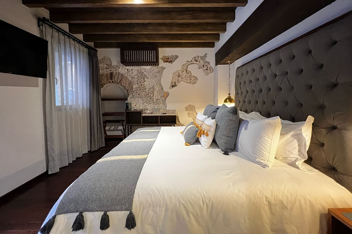Ein Schlafzimmer mit einem großen Bett, einer Wandmalerei aus Stein, einer Holzbalkendecke und einem Schreibtisch mit einer Lampe.