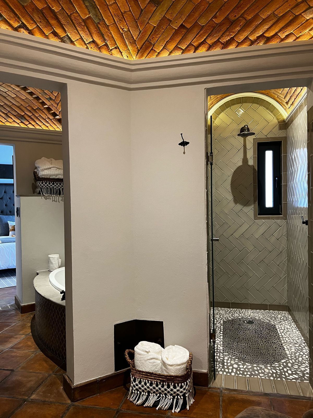 A bathroom with a herringbone-patterned shower wall, a white sink, and a wicker basket with towels.