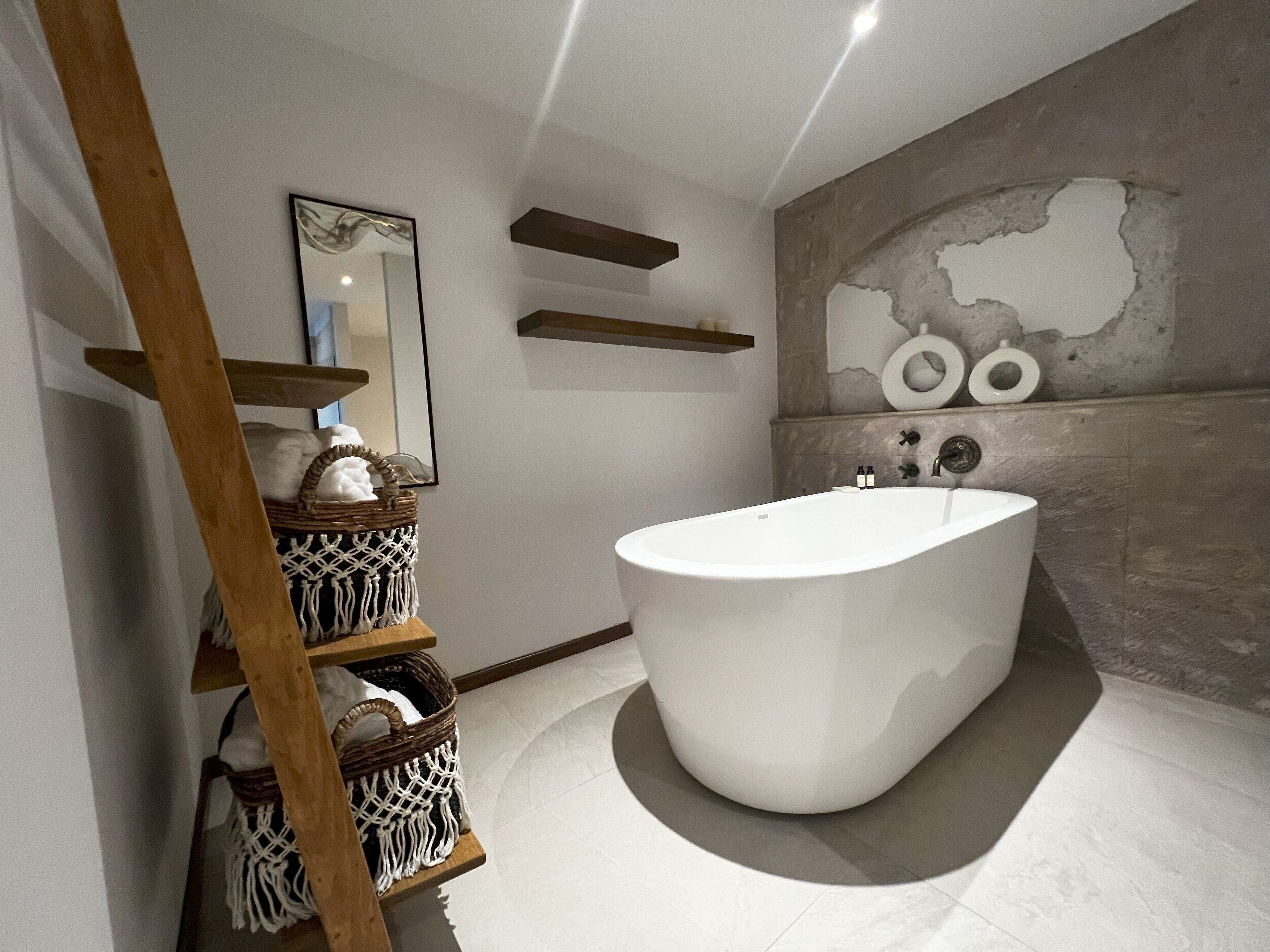 Ein modernes Badezimmer mit freistehender Badewanne, Holzregalen und einer Wanddekoration aus Makramee.