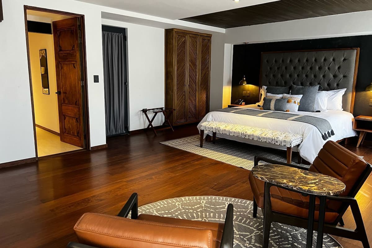 Ein modernes Hotelzimmer mit einem großen Bett, einem kleinen runden Tisch, Ledersesseln und einem Holzschrank.