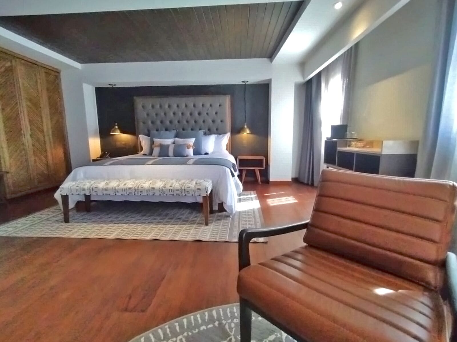 Un dormitorio moderno con una cama grande, un armario de madera, una zona de estar y una mesita.