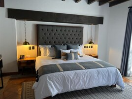 Un dormitorio con cabecera capitonada, una cama con ropa de cama blanca y gris, dos mesitas de noche con lámparas y una alfombra estampada.