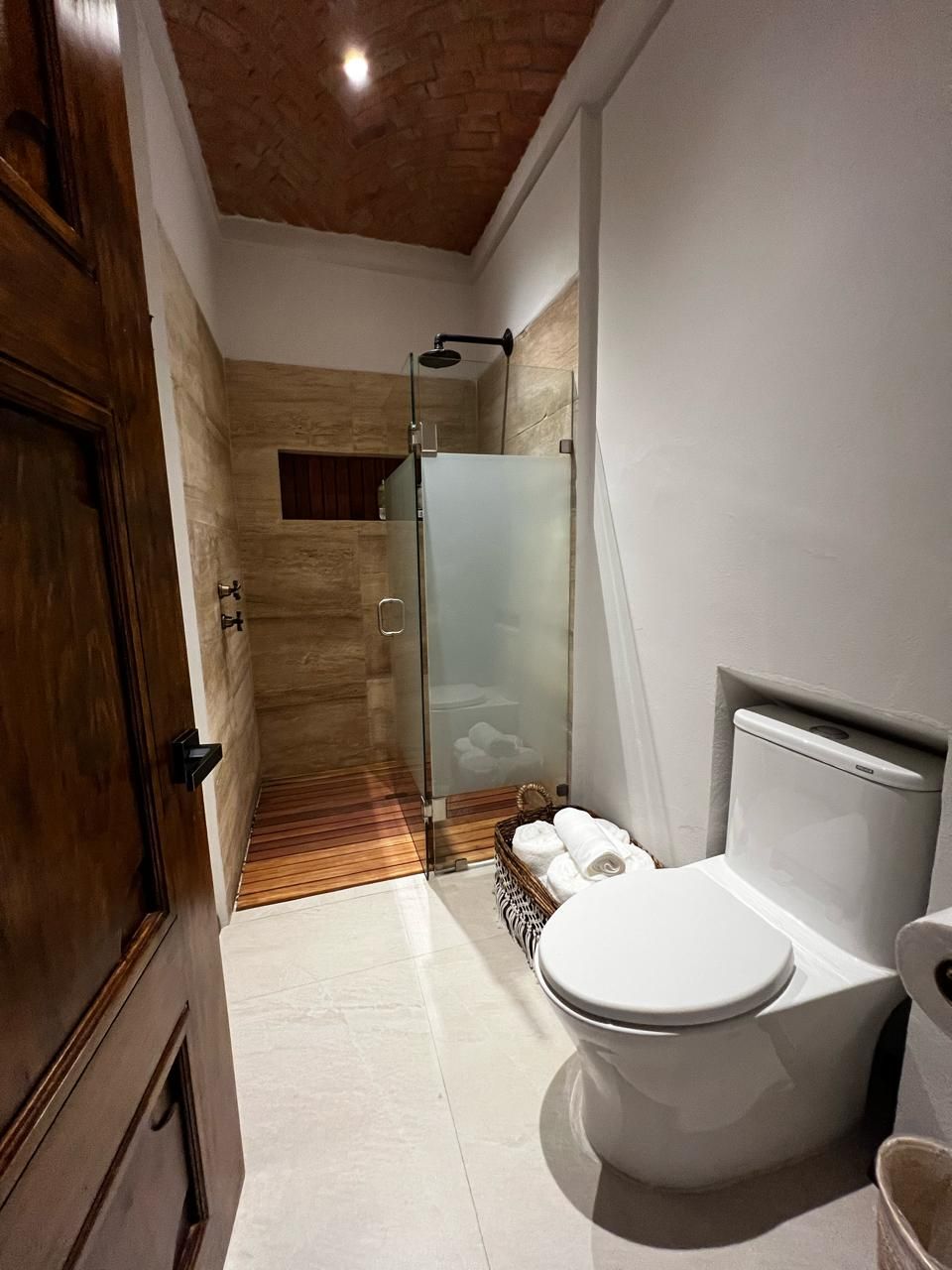 Un baño con puerta de madera, cabina de ducha de vidrio, inodoro y bidé.